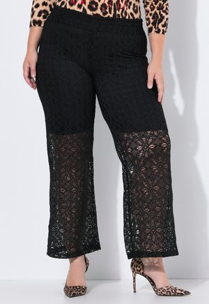 Pantalones de encaje negro de crochet con corte de pierna ancha, que presentan patrones florales y una cintura sólida. Combinados con tacones de estampado de leopardo.