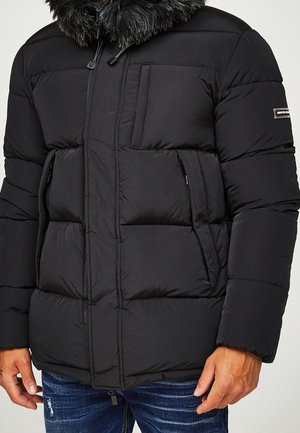 Sort polstret jakke med hætte foret med pels, med lynlåse og klaplommer, der har et quiltet design og tekstureret overflade.