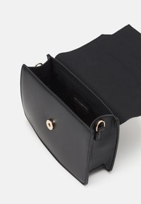 Sac en cuir noir avec quincaillerie dorée, un extérieur lisse, un compartiment unique et une fermeture à pression. Présente un intérieur doublé en tissu.