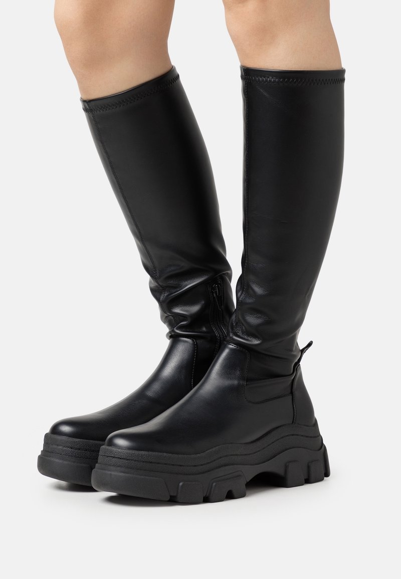 Bottes noires montantes en cuir lisse, dotées d'une semelle plateforme épaisse, d'une fermeture éclair latérale et d'accents cousus en haut.