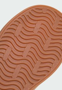 Gros plan d'une semelle de chaussure marron avec des rainures ondulées et des sections de grip rectangulaires texturées pour la traction.