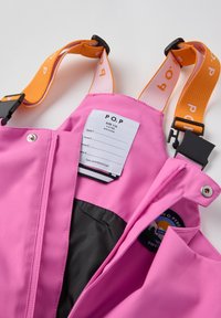 Vaaleanpunaiset vedenpitävät haalari, joissa on säädettävät oranssit hihnat, vetoketjullinen etuosa ja musta vuori. Varustettu tarralla koon ja hoito-ohjeiden ilmoittamiseksi.