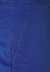 Tissu bleu avec une texture diagonale, présentant une couture et une ceinture plate. Le tissu semble lisse et durable. Aucun motif ou accent visible.