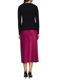Zwarte lange mouwen top gecombineerd met een knielange, glanzende fuchsia satijnen rok. De outfit heeft een getailleerde pasvorm en wordt aangevuld met zwarte hakken.