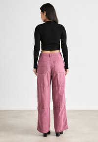 Top court noir à côtes et pantalon large taille haute en tissu rose doux. Les pantalons possèdent deux poches arrière et des coutures contrastantes.