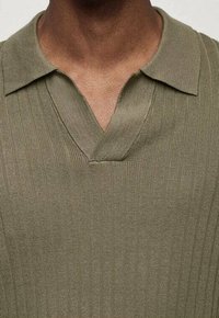 Oliivinvihreä neulottu pikeepaita, jossa on ribatoitu pinta, V-pääntie ja lyhyt kaulus. Kangas näyttää pehmeältä ja kevyeltä.