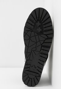 Zwarte schoenzool met geometrische en kruisvormige profielpatronen en de merknaam "Marc Cain" gebosst nabij de hiel.