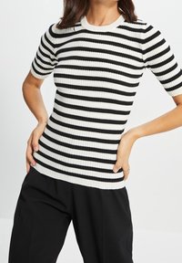 Schwarz-weiß gestreiftes kurzärmeliges, geripptes Stricktop mit rundem Halsausschnitt und figurbetonter Silhouette, kombiniert mit dunkler Hose.