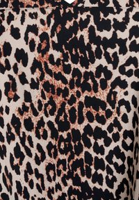 Tkanina w cętkę lamparta z jasnobeżowym tłem i czarnymi oraz brązowymi plamami, prezentująca teksturowany i zróżnicowany wzór.