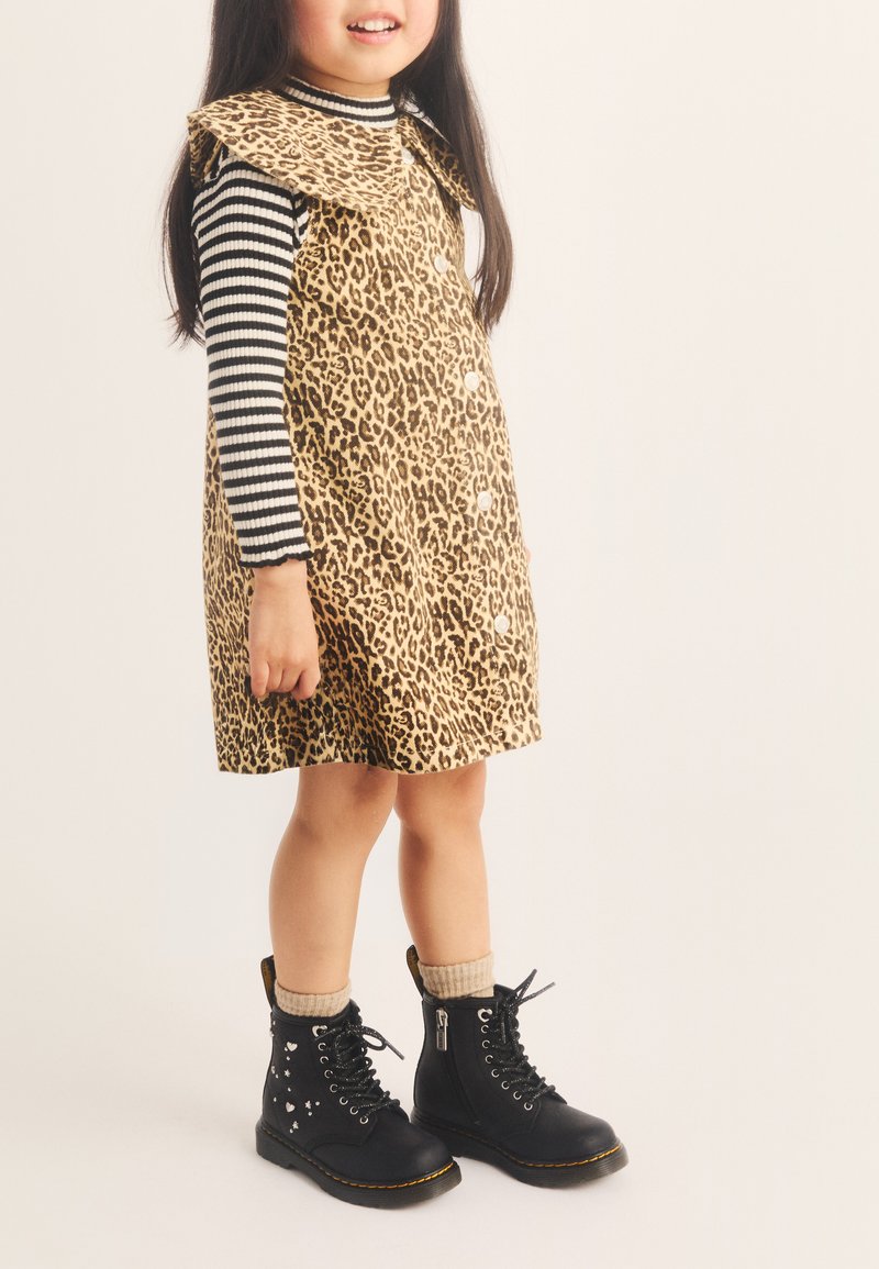 Jeune fille portant une robe à imprimé léopard sur un t-shirt à manches longues rayé noir et blanc, des chaussettes beige et des bottes noires à lacets avec des détails en forme de cœur.