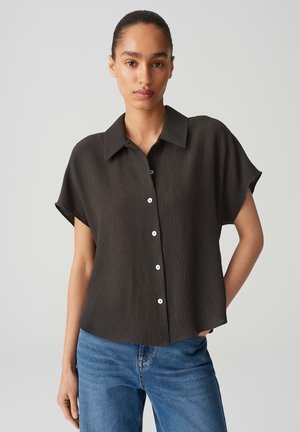 Black textured short-sleeve shirt with a collared neckline and white buttons, paired with blue jeans. Simple, relaxed fit design.