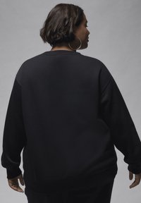 Sort sweatshirt med en afslappet pasform, ribbede manchetter og rund halsudskæring. Blød tekstur og minimalistisk design, vist fra ryggen.