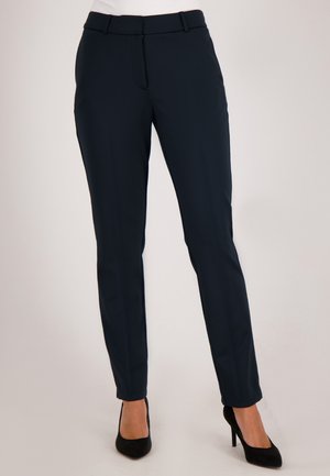Navy tailored trousers met een slim fit, voorzien van een gladde textuur, riemlussen en zijzakken, gecombineerd met zwarte hoge hakken.