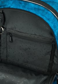 Interno di uno zaino in tessuto nero con una tasca con zip. Presenta un motivo texturizzato nero e un esterno blu in contrasto nella parte superiore.