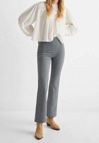 Vit, strukturerad långärmad blus i kombination med högmidjade byxor med svart-vit mönster och beige ankelskor.