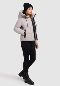 Polstret, lys grå jakke med hætte, forlommer og sorte detaljer. Bæres med sorte leggings og kraftige sorte støvler.