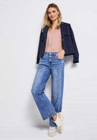 Marinblå kort jacka över en ljusrosa linne, kombinerad med lösa blå denimjeans och vita sneakers med beige detaljer. Enkel design.
