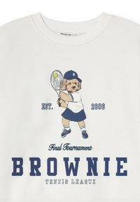 Perro pequeño con atuendo de tenis sosteniendo una raqueta y golpeando una pelota de tenis, con el texto "EST. 2006," "Torneo Final" y "Liga de Tenis BROWNIE."