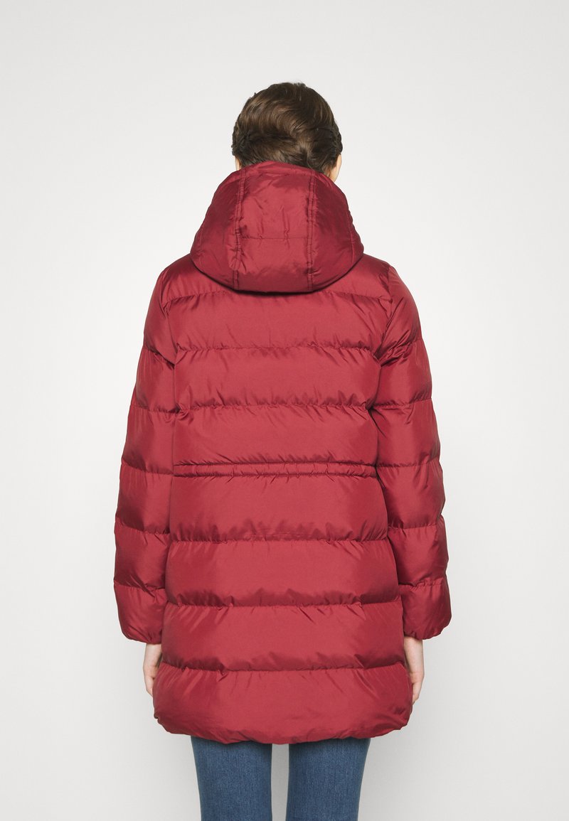 Cappotto puffer rosso lungo con cappuccio, caratterizzato da sezioni trapuntate, un'esterno liscio e un design di lunghezza media che si ferma sopra i fianchi.