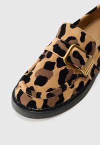 Leopardmønstrede loafers i ruskind med en guldspænde og en sort gummisål. Accenter af tan, sort og brun i mønsteret.