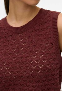 Gros plan d'une femme portant un haut sans manches bordeaux en maille avec un motif de losanges ajourés texturé.