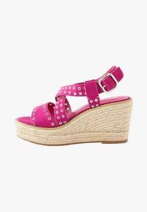 Sandale compensée en cuir suédé rose avec des brides croisées, des accents en œillets argentés et une plateforme en jute tressé. Bride de cheville ajustable avec boucle.