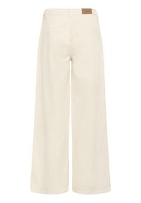 Pantalon à jambes larges de couleur crème avec des poches fendues à l'arrière et une petite étiquette de marque en cuir marron sur la ceinture.