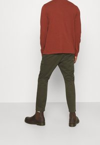 Långärmad rostfärgad skjorta som kombineras med olivgröna snäva byxor och mörkbruna ankelskor, med en slät ytstruktur och enkel design.