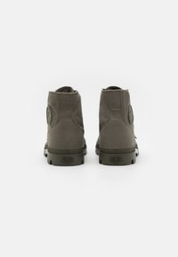 Botas de tobillo de lona verde con punta redonda, suela de goma y parche de logo lateral, que presentan detalles de costura y un exterior texturizado.