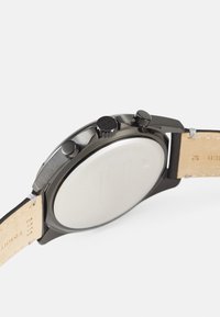 Montre chronographe noire avec un boîtier en acier inoxydable, finition polie, couronne texturée et un bracelet en cuir beige avec un intérieur lisse.
