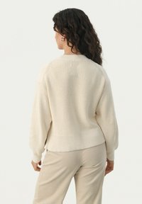 Crème kleurige geribbelde gebreide trui met lange mouwen, ronde halslijn en een ontspannen pasvorm. Gepaarde met lichtbruine corduroy broek.