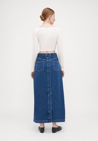 Blå denim maxiskjørt med høy midje, to baklommer og en sentral søm. Kombinert med en tettsittende hvit langermet topp.