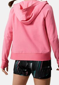Sudadera con capucha rosa con cordón ajustable, tejido suave y puños acanalados. Combinada con pantalones cortos negros que presentan un patrón abstracto colorido.