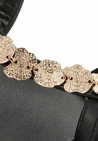 Correa de cuero negro con adornos metálicos en tono dorado decorativos en forma de monedas, que presentan patrones intrincados y detalles texturizados.