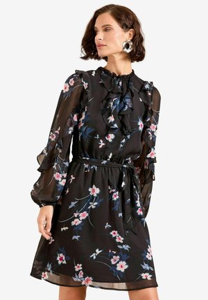 Abito nero a fiori realizzato in tessuto trasparente, con dettagli arricciati, maniche lunghe a sbuffo e vita legata. Motivi floreali in rosa e blu.