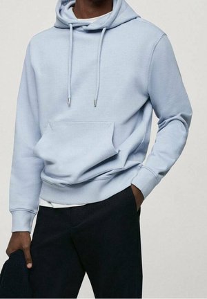 Felpa azzurra chiara realizzata in tessuto morbido, con tasca a marsupio frontale, cordini e polsini a costine. Indossata con pantaloni scuri.