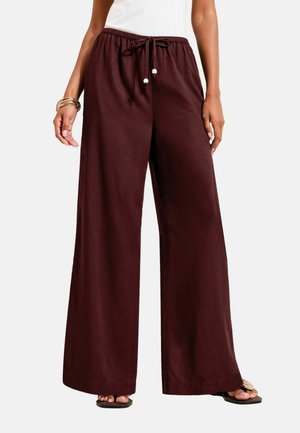 Loose-fitting wide-leg burgundy pants with elastic waist and drawstring, worn with white top and sandals.