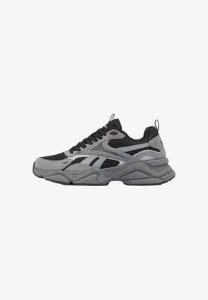 Zapatilla deportiva negra y gris con paneles de malla y ante, cierre de cordones y suela gruesa moteada, vista lateral sobre fondo blanco.