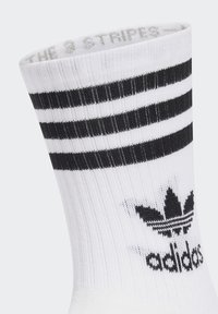 Fehér pamut zokni, amelyen három vízszintes fekete csík található a tetején, valamint egy fekete adidas logó egy levél design felett az oldalon.