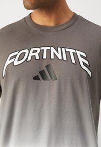 Grå bomulds t-shirt med hvid "FORTNITE" tekst og et sort adidas logo centreret nedenfor, med en glat tekstur og korte ærmer.