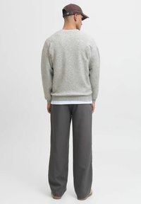 Grå strikket sweater med en afslappet pasform, ribbede manchetter og kant. Kombineret med løstsiddende mørkegrå bukser og en brun kasket.