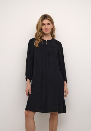 Vestido negro hasta la rodilla con un corte suelto, mangas tres cuartos, escote redondo y una textura de cuadrícula sutil. Detalle de ojal en el cuello.
