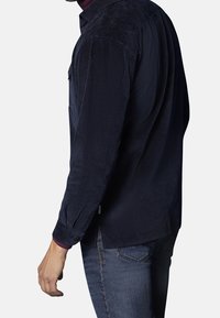 Camisa de pana azul marino con cuello abotonado, manga larga y textura acanalada visible; presenta una sutil abertura en el dobladillo y puños abotonados.