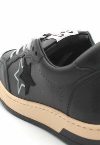 Sneaker in pelle nera con una stella nera testurizzata e accenti di stella grigia, lacci bianchi e suola beige. Presenta una linguetta imbottita e dettagli di cucitura.
