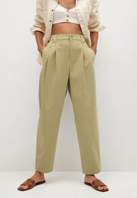 Pantalons taillés en vert olive clair avec des plis, des poches latérales et une coupe décontractée. Associés à des sandales à glissière marron et un top court.