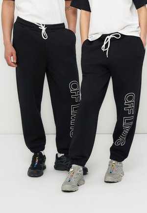 Dve osebi, oblečeni v črne športne hlače z belo napisano besedno zvezo »OFF LIMITS« na hlačnicah, z belimi vrvicami, belimi zgornjimi deli oblačil in črno-sivimi športnimi copati.