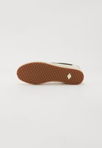Sneaker mit einer beigen Gummisohle, die mit einem Diamantmuster strukturiert ist. Schwarzer oberer Bereich mit einem kleinen Logo-Akzent. Flaches, lässiges Design.