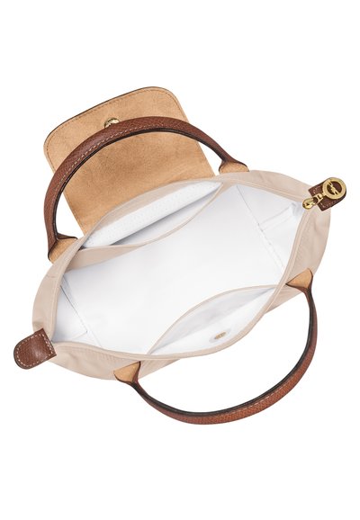 Beige bag with brown leather handles and a suede flap. Interior features white lining and one zipper pocket. Bag is soft and structured.