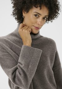 Taupe turtleneck sweater in soft, textured fabric with ribbed cuffs. Features a relaxed fit and high neckline.