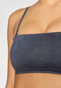 Σκούρο γκρι, ελαστικό μπραλέτ με λεπτές τιράντες, αδιάκοπη σχεδίαση και μαλακή, λεία υφή. Κλασικό, μινιμαλιστικό στυλ.